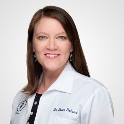 A professional portrait of a smiling woman wearing a white veterinarian's coat with a name tag reading "Dr. Barbara Holladay." She has long brown hair and earrings, against a light gray background.