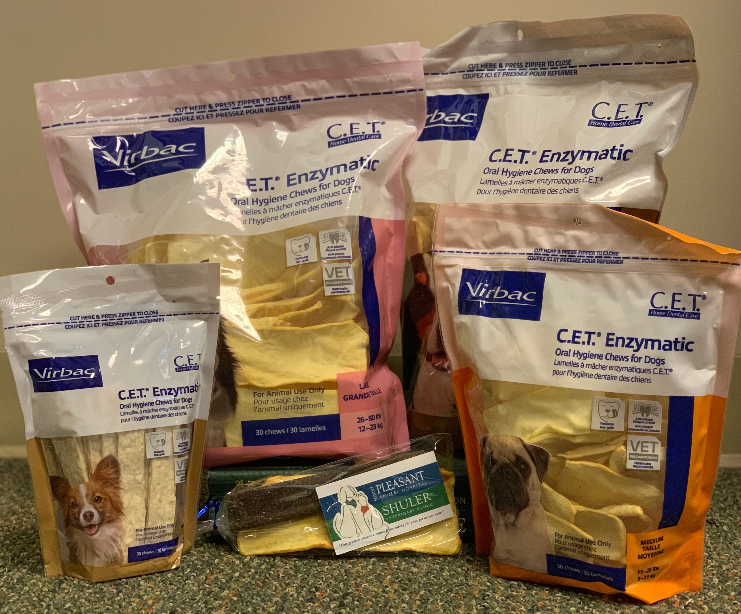 Various bags of Virbac C.E.T. enzymatic oral hygiene chews for dogs, recommended by a vet and displaying different flavors and sizes, arranged on a carpeted floor.