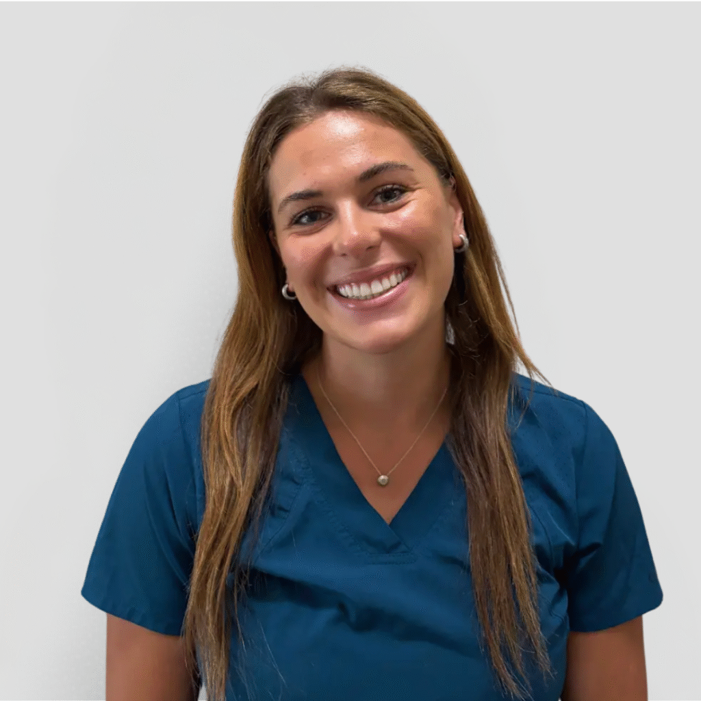 A veterinarian wearing a blue scrub top and smiling gently against a plain white background.