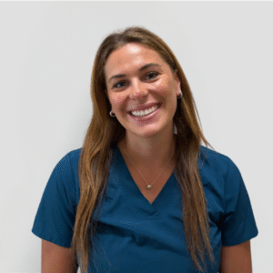 A veterinarian wearing a blue scrub top and smiling gently against a plain white background.