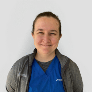 A veterinarian wearing a blue scrub top and smiling gently holding a cat against a plain white background.