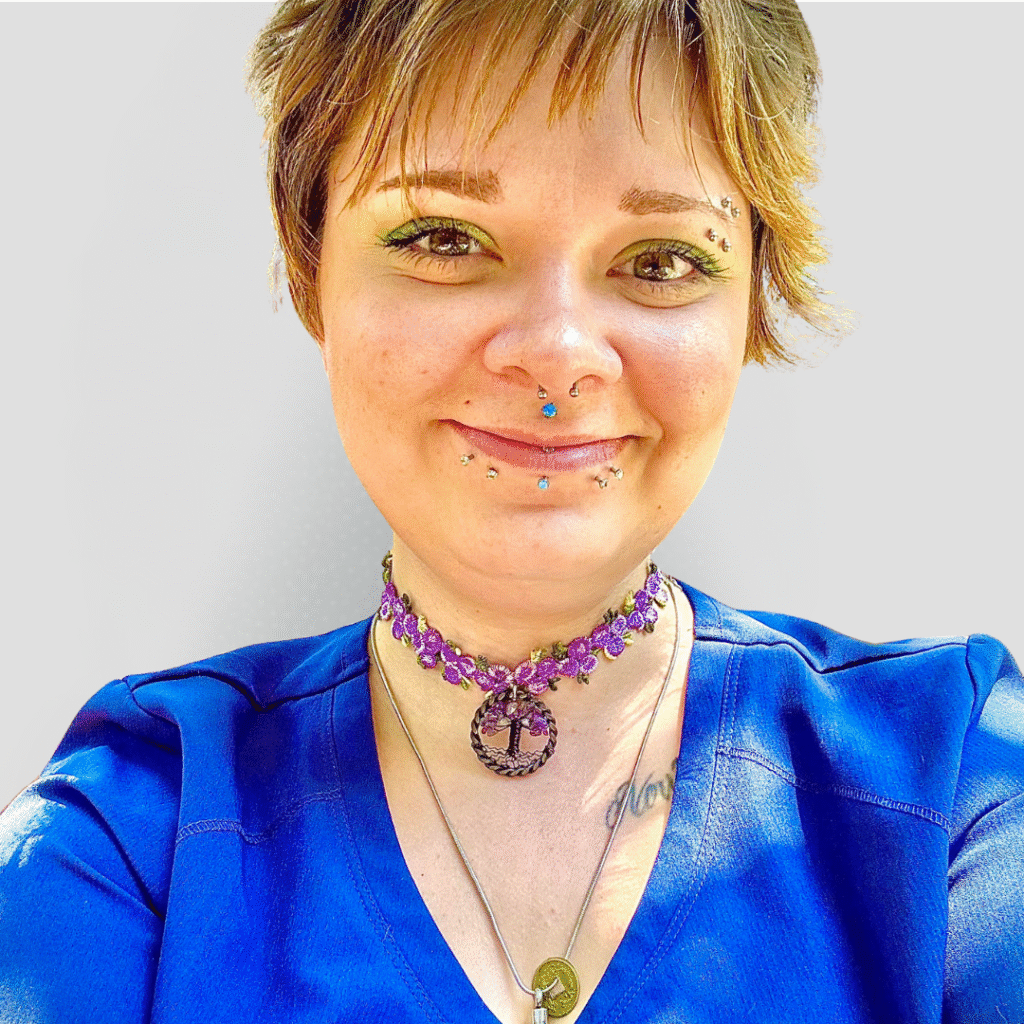 A veterinarian wearing a blue scrub top and smiling gently against a plain white background.