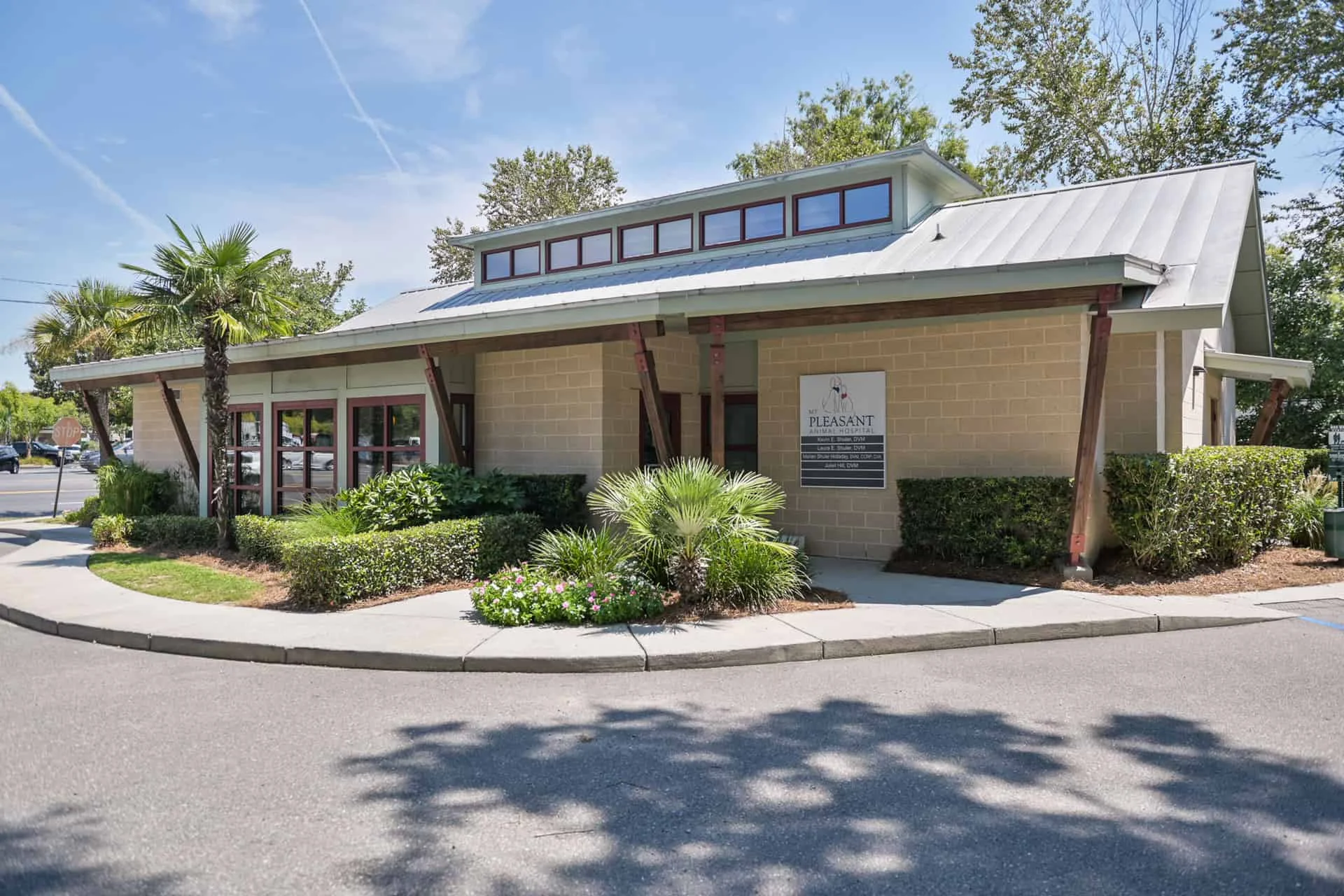 Modern single-story veterinarian clinic with a large entrance sign, surrounded by well-maintained landscaping and palm trees under a clear blue sky.